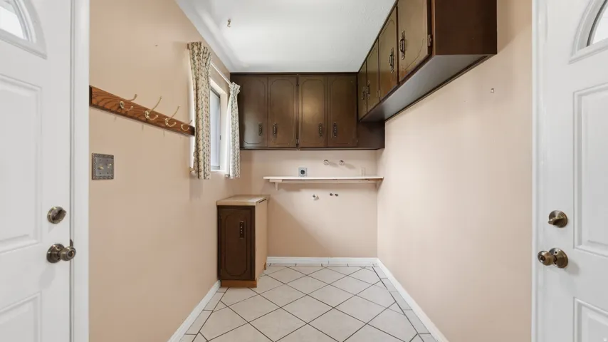 Utility space featuring a window, built-in upper cabinetry, a base cabinet, tiled flooring, and a wall-mounted coat rack
