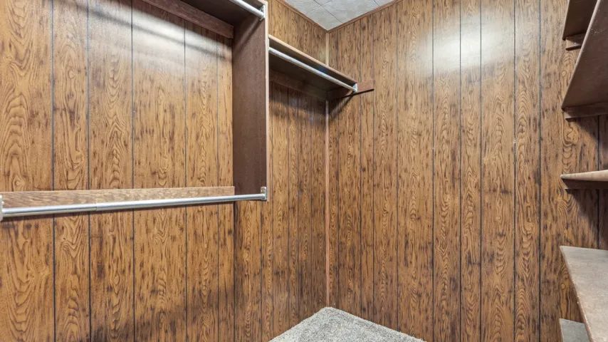 Closet featuring wood-panel walls, carpet flooring, a built-in shelf unit, and multiple clothing rods