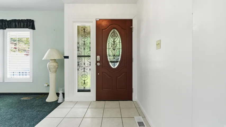 Entryway featuring a wood-panel door with an oval stained-glass insert, sidelight with decorative ironwork, and light-toned square tile flooring