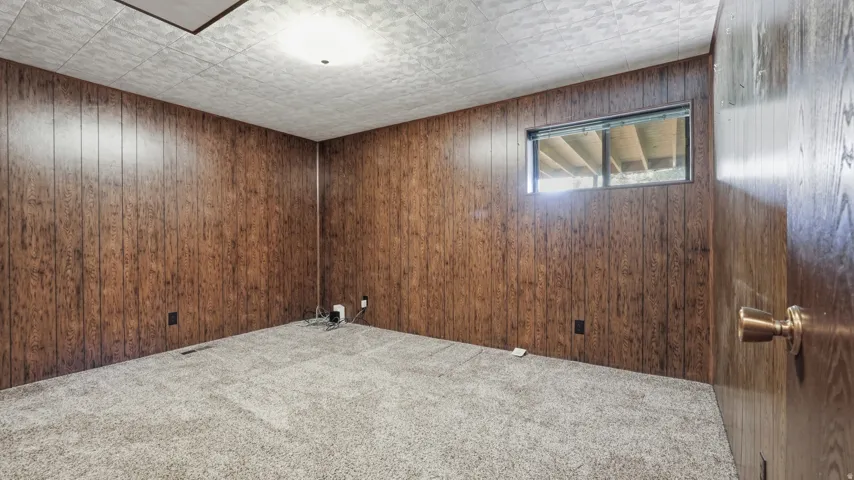 Room featuring full wood paneling, light gray carpeting, and a window