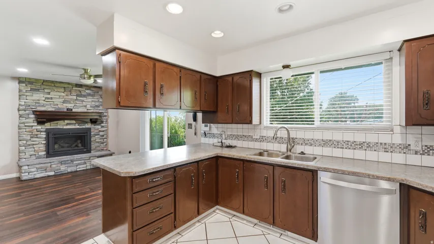 Kitchen featuring wood-finish cabinetry, light-toned countertops, a stainless steel double sink, and an integrated stainless steel dishwasher