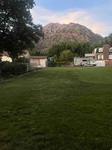 Expansive lawn with mature perimeter trees, a detached storage building, and a mountain backdrop
