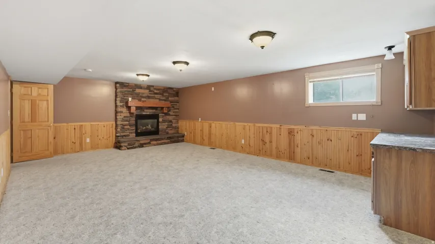 Spacious lower-level room featuring a stacked stone fireplace with a wood mantel