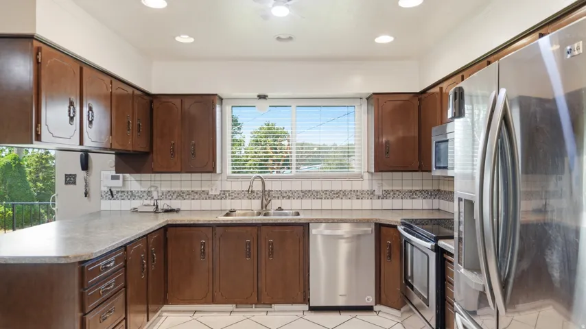 Kitchen featuring wood cabinetry, stainless steel appliances, a double basin sink, light-toned countertops, and a tiled backsplash