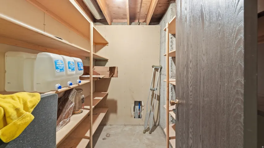 Basement utility room featuring exposed ceiling joists, concrete flooring, built-in shelving, and a wood-finish door