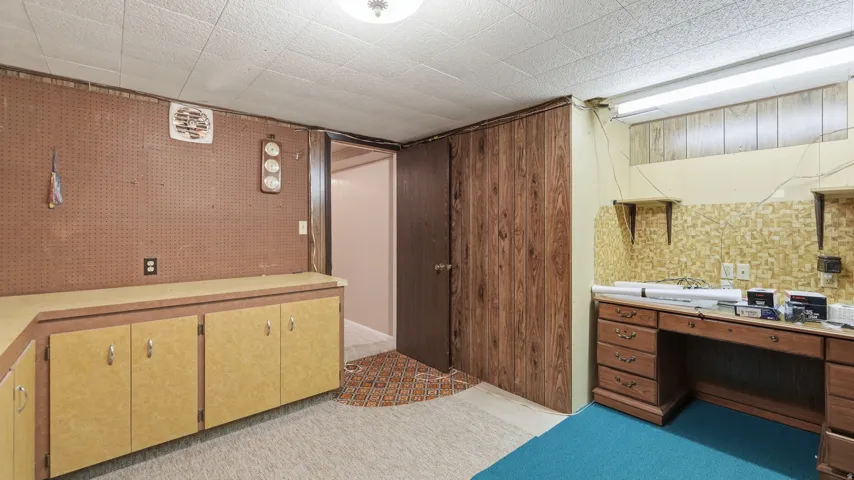 Utility room featuring extensive built-in cabinetry with laminate countertops, pegboard wall storage, and a dedicated workspace with a built-in desk