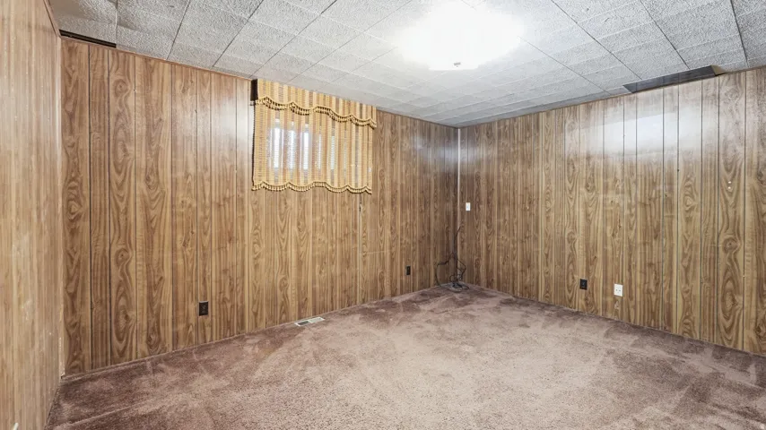 Room featuring wood-finish paneling, a drop ceiling with recessed lighting, and carpeting