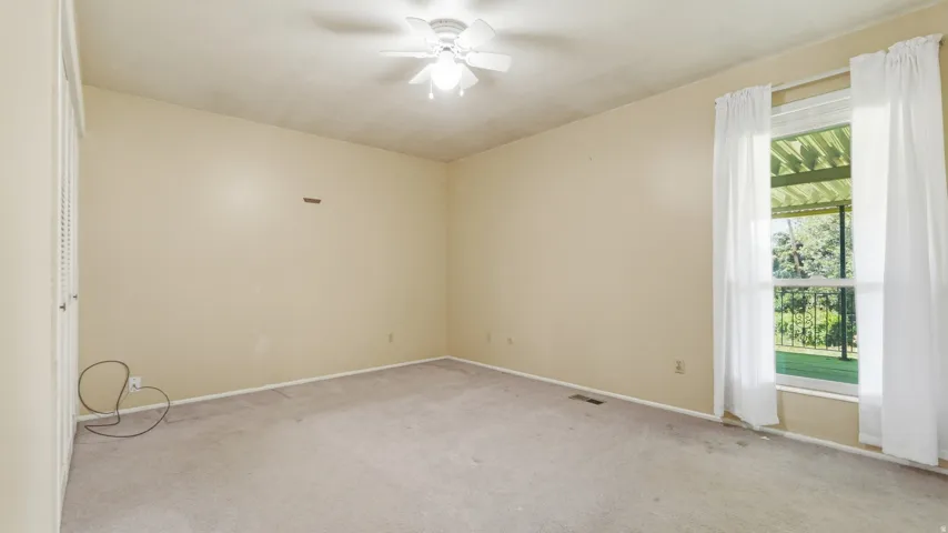 Carpeted interior space featuring a window with white drapes, a ceiling fan, and a bi-fold closet