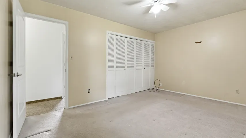 Carpeted room featuring a ceiling fan, bifold closet doors, and light-toned walls