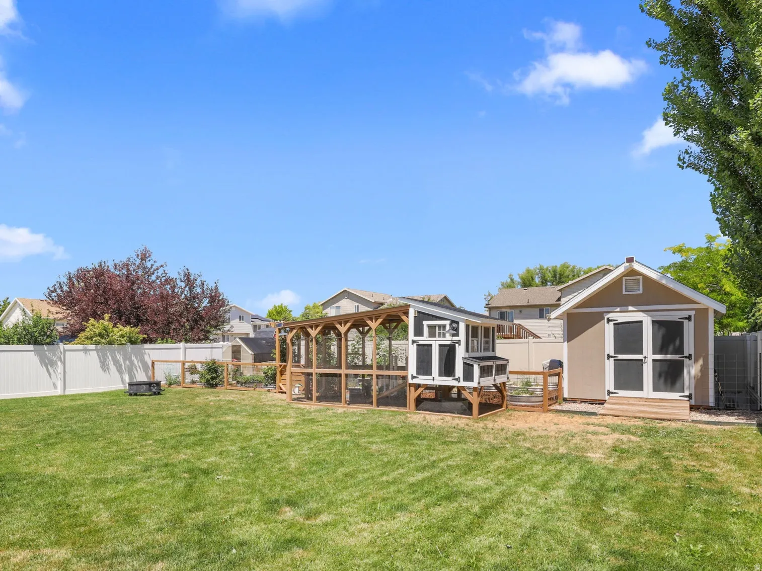 Expansive green lawn featuring a substantial storage shed with double doors, an enclosed chicken coop structure, and a perimeter white vinyl fence