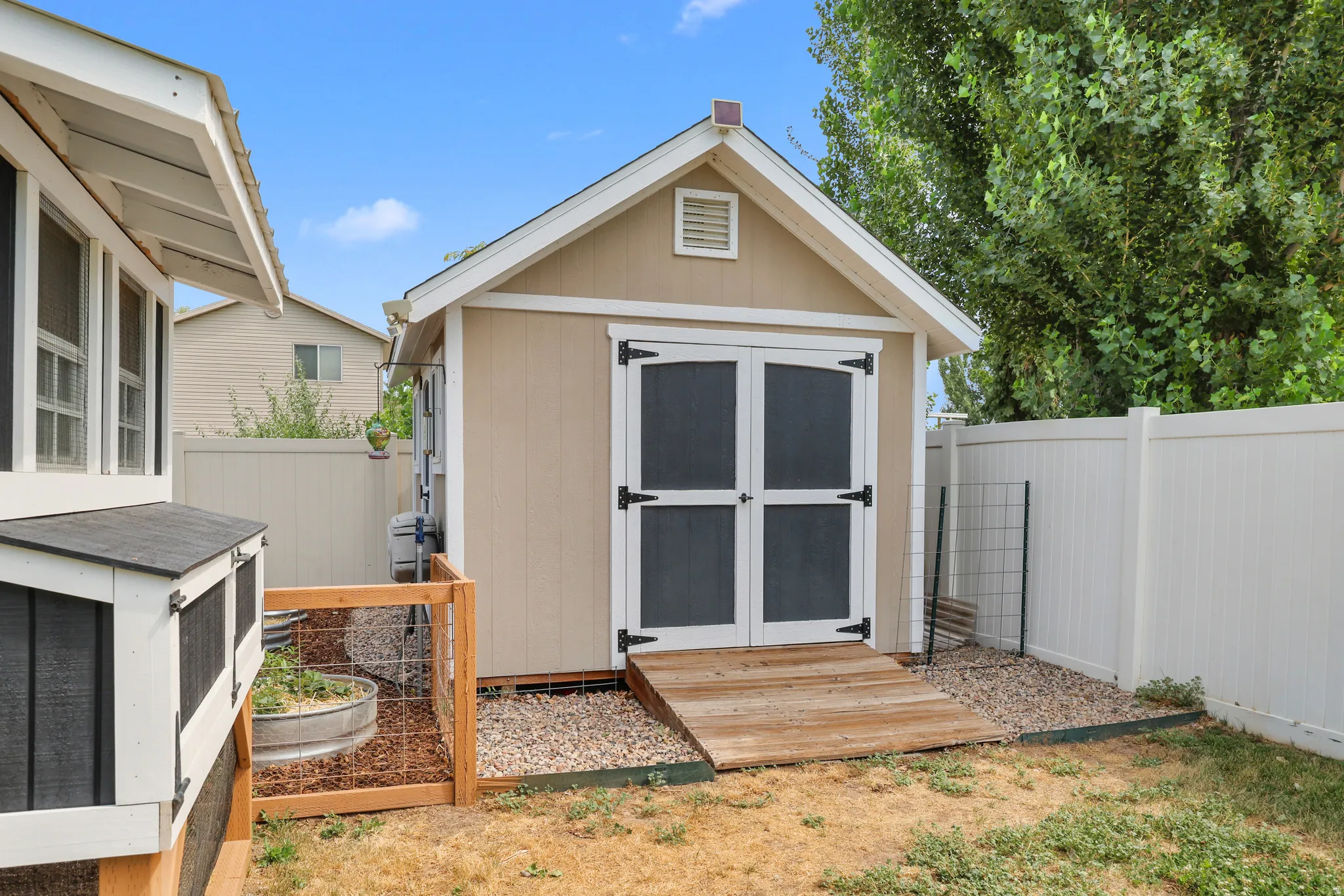 Custom storage shed with beige siding and white trim, featuring double screen doors and an access ramp