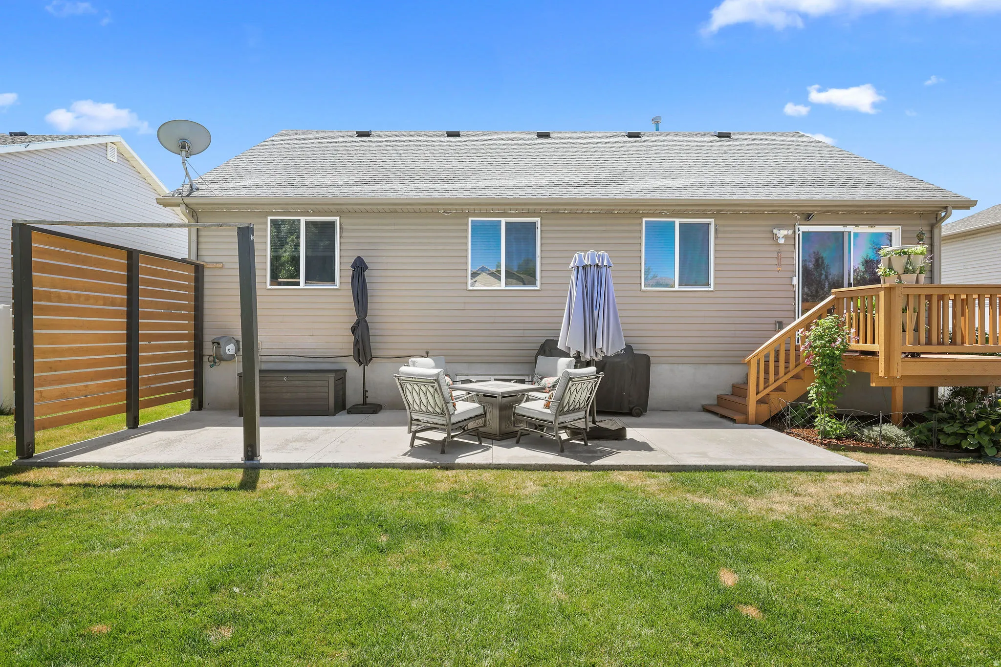 Expansive backyard featuring a concrete patio, a wood privacy screen, and a wood deck with stairs