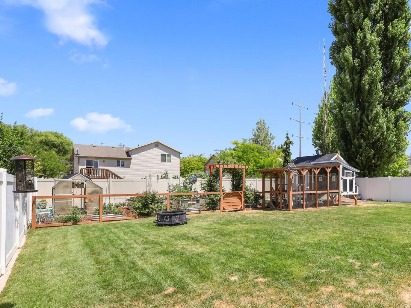 Expansive backyard featuring a large lawn, a white privacy fence, a dedicated gardening area with a greenhouse, and an additional outdoor structure