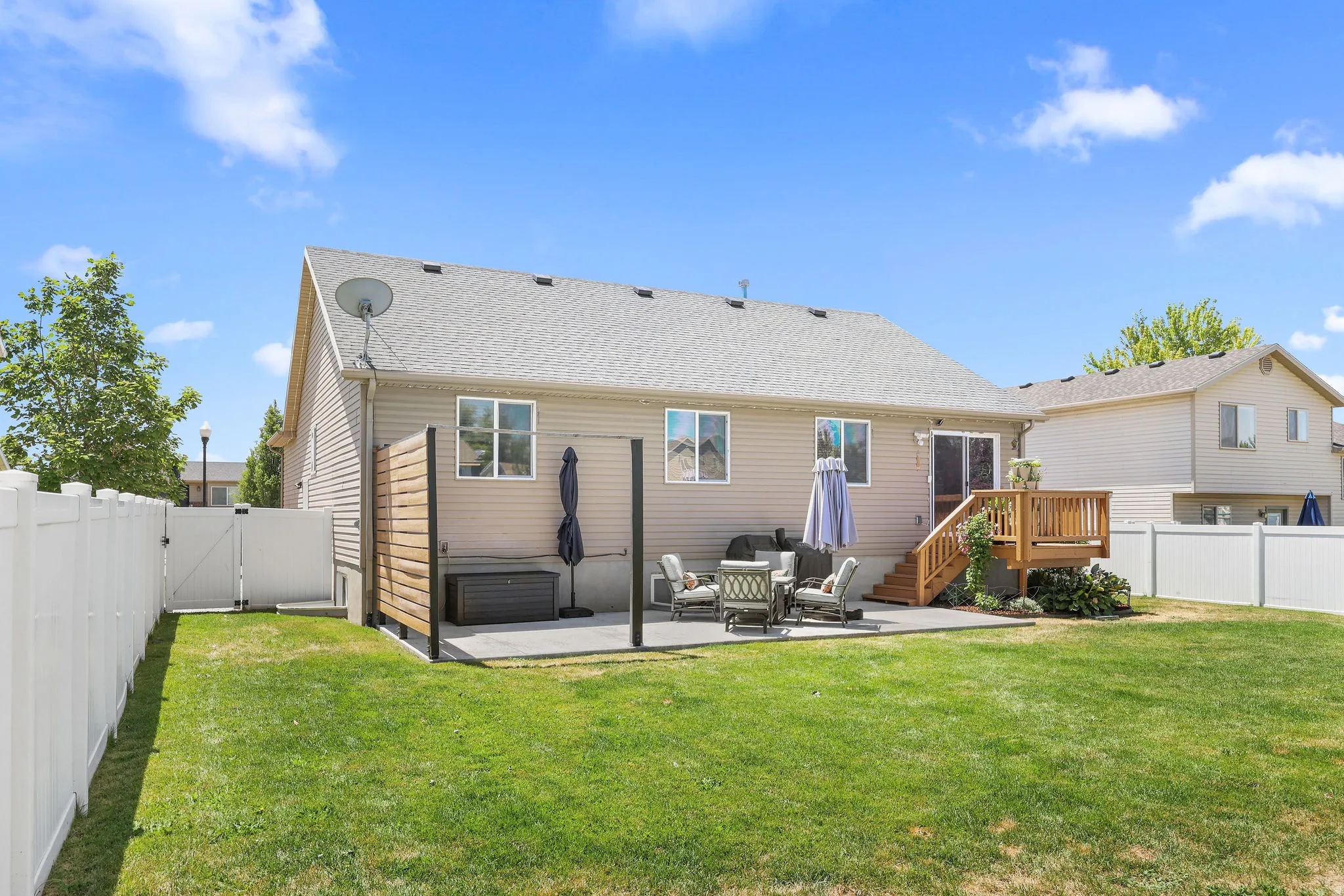 Spacious backyard featuring a manicured lawn, white vinyl fencing, a concrete patio, and a wood deck with stairs