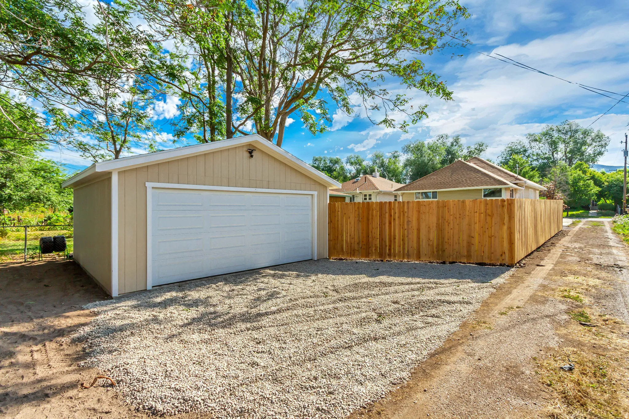 Detached garage with a white panel door, light tan siding, and white trim