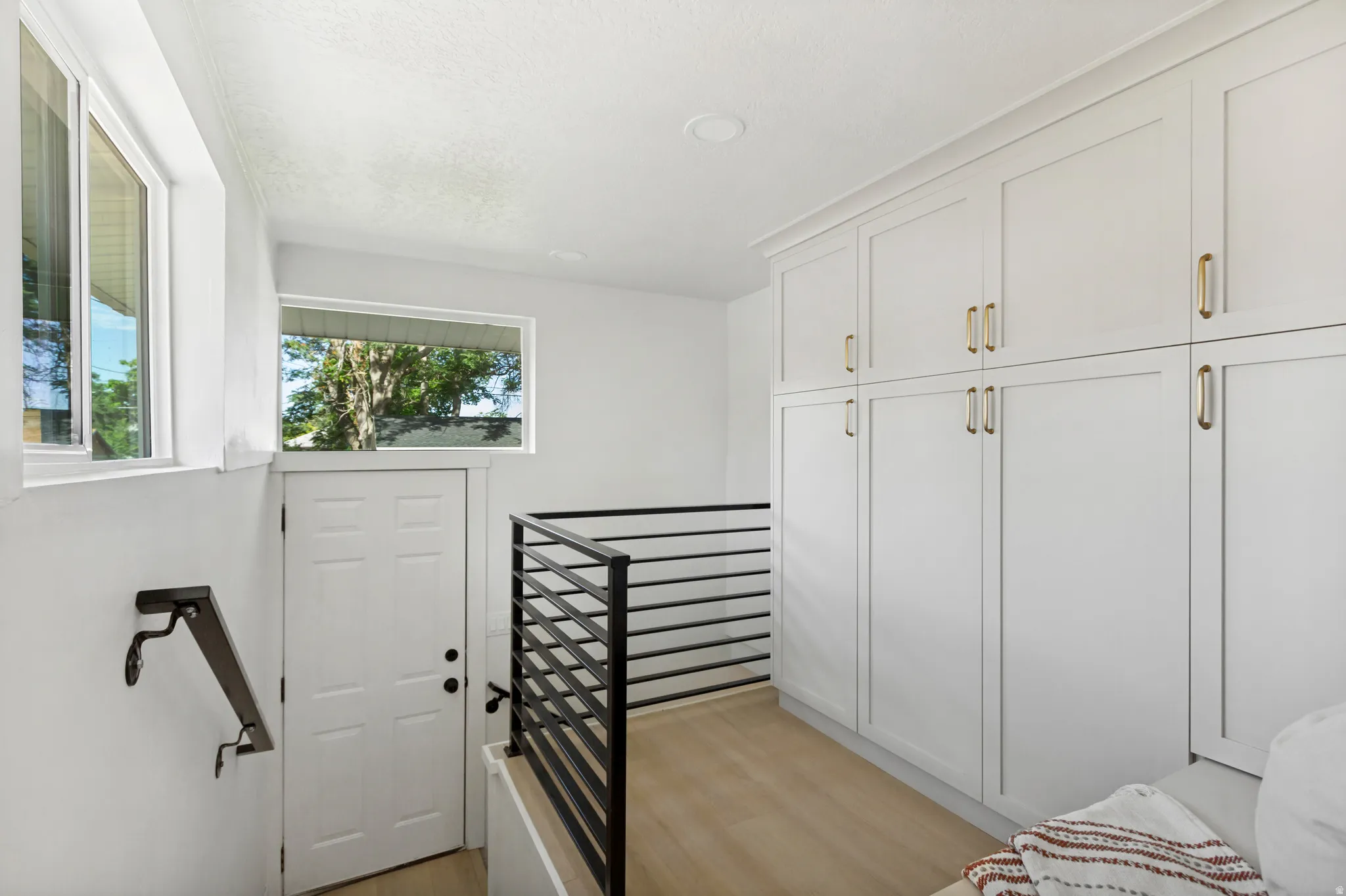 Built-in white cabinetry with gold-finish hardware and crown molding, wood-finish flooring, recessed lighting, and a modern horizontal bar railing