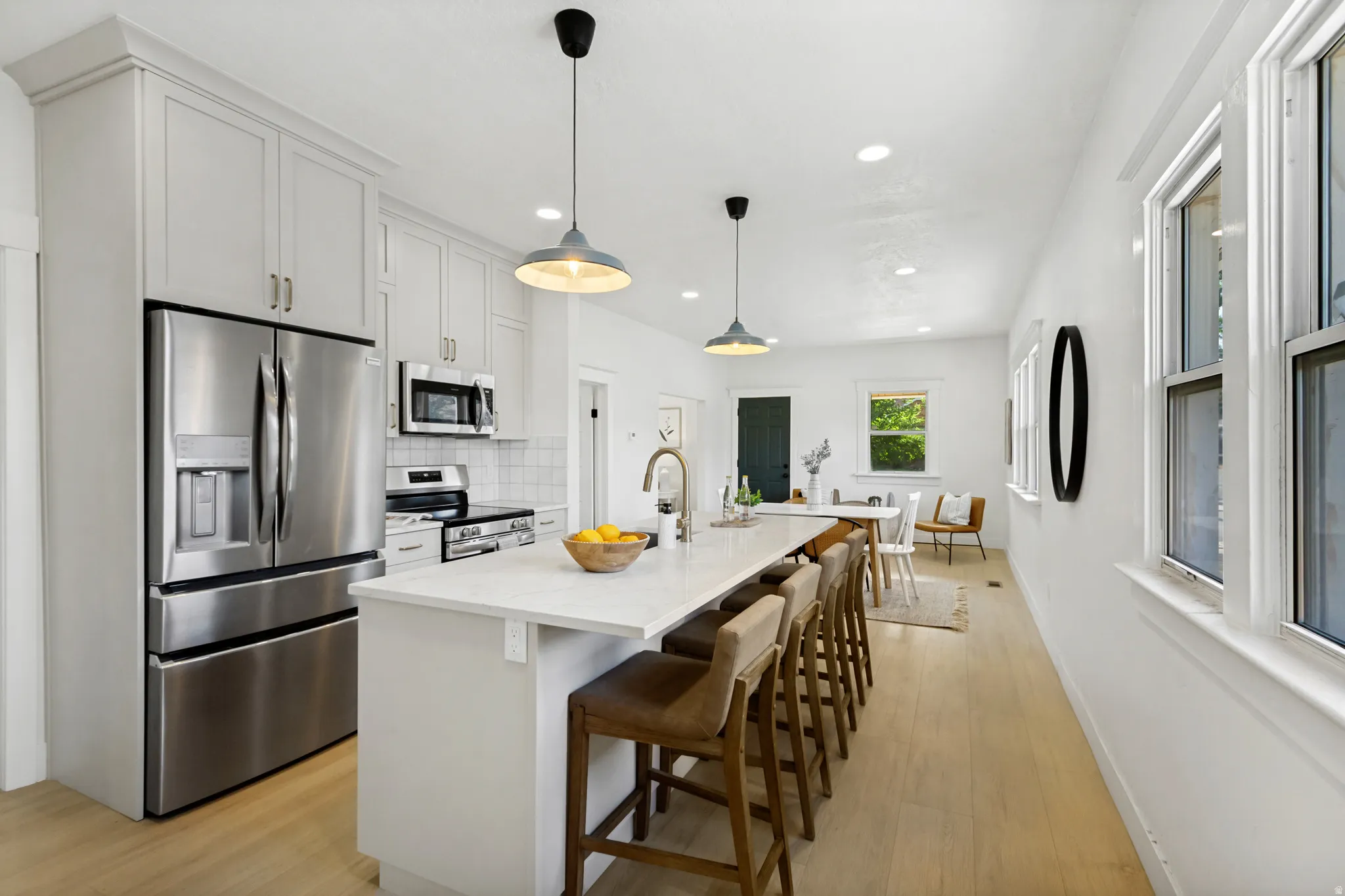 Contemporary kitchen featuring an expansive island with seating, stainless steel appliances, white shaker cabinetry, and light wood-finish flooring
