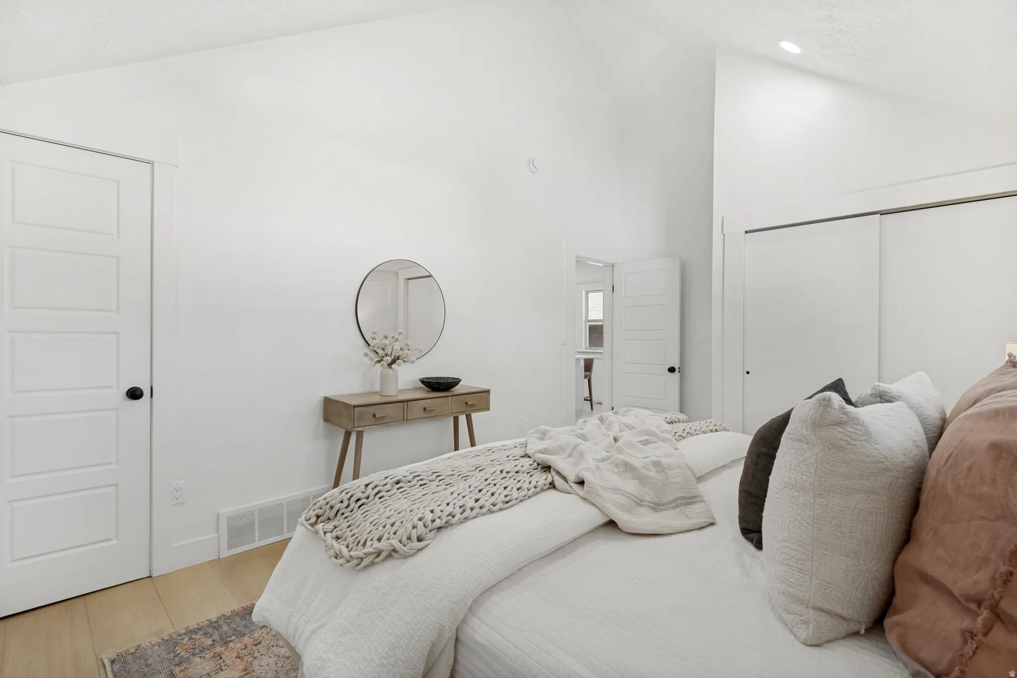 Vaulted ceiling bedroom featuring white walls, five-panel interior doors with black hardware, wood-finish flooring, and sliding closet doors