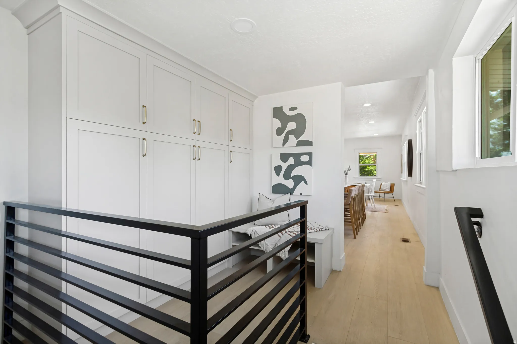 Hallway featuring extensive built-in cabinetry with gold-tone hardware, wood-finish flooring, and a modern horizontal slat railing