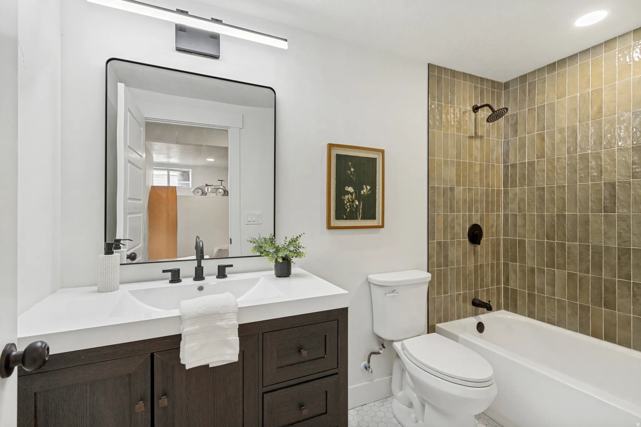 Contemporary bathroom featuring a dark wood-finish vanity with an integrated dual sink countertop, a large framed mirror, and matte black fixtures
