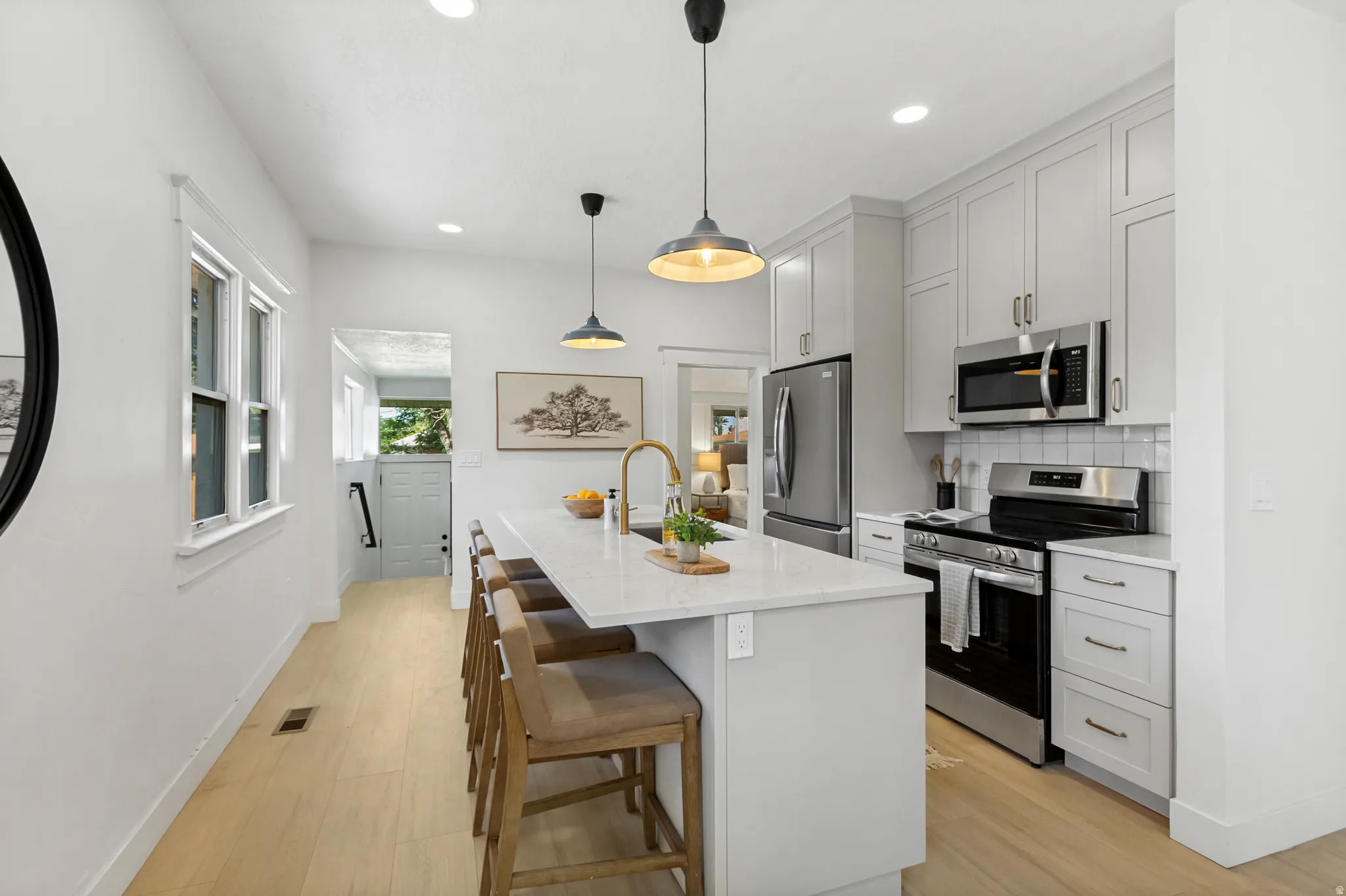 Kitchen featuring a central island with countertop seating, light-toned cabinetry, stainless steel appliances, and wood-finish flooring
