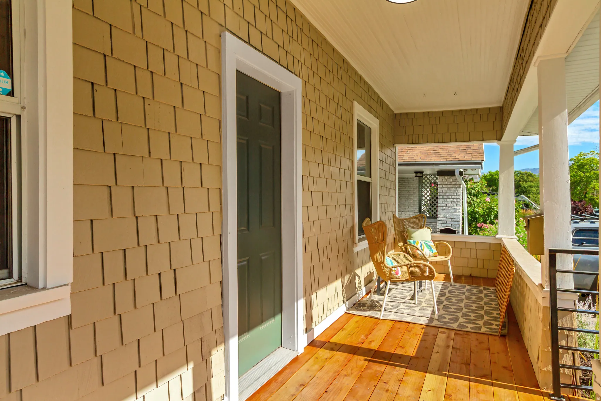 Covered front porch featuring wood-finish flooring, cedar shake siding, white trim, and a black paneled door