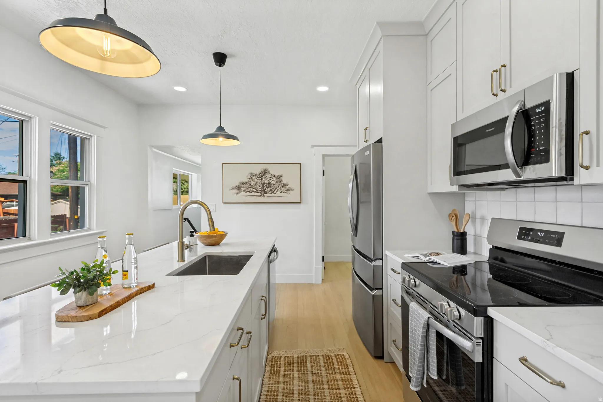 Kitchen featuring white shaker cabinetry, stainless steel appliances, light wood-finish flooring, and white countertops with a subtle gray vein