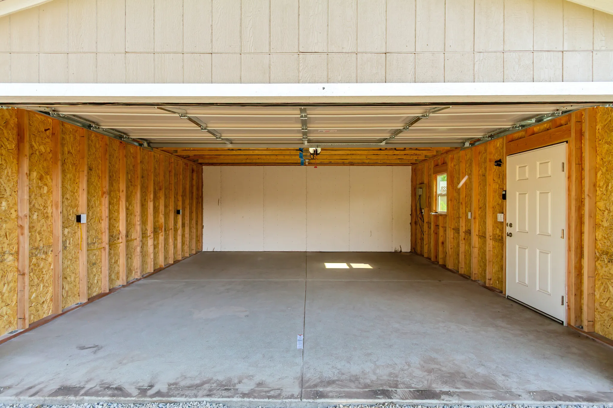 Spacious garage with exposed wood-finish wall framing, concrete flooring, and a white interior door