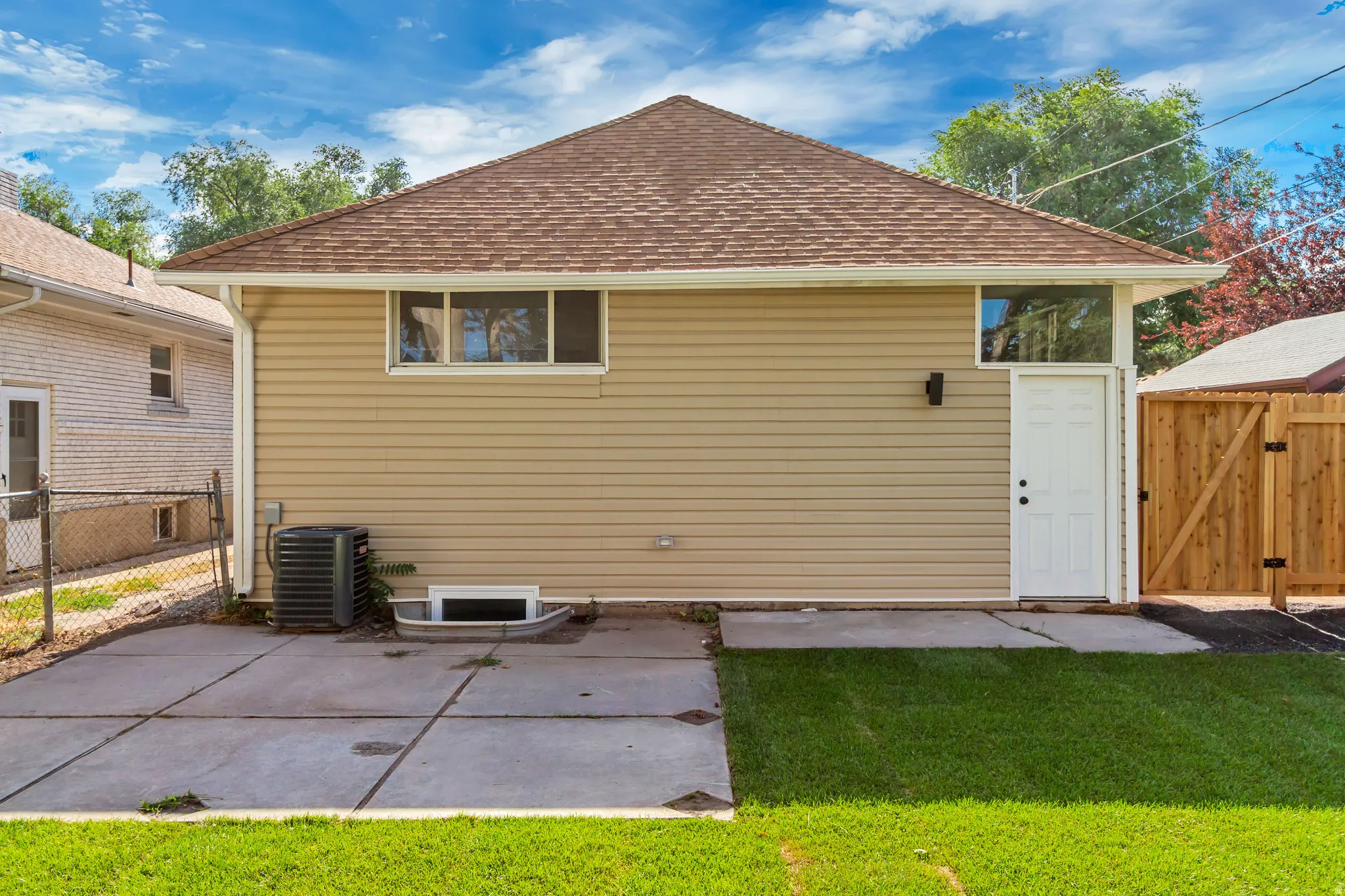 Rear exterior featuring beige siding, a brown shingle roof, and a concrete patio