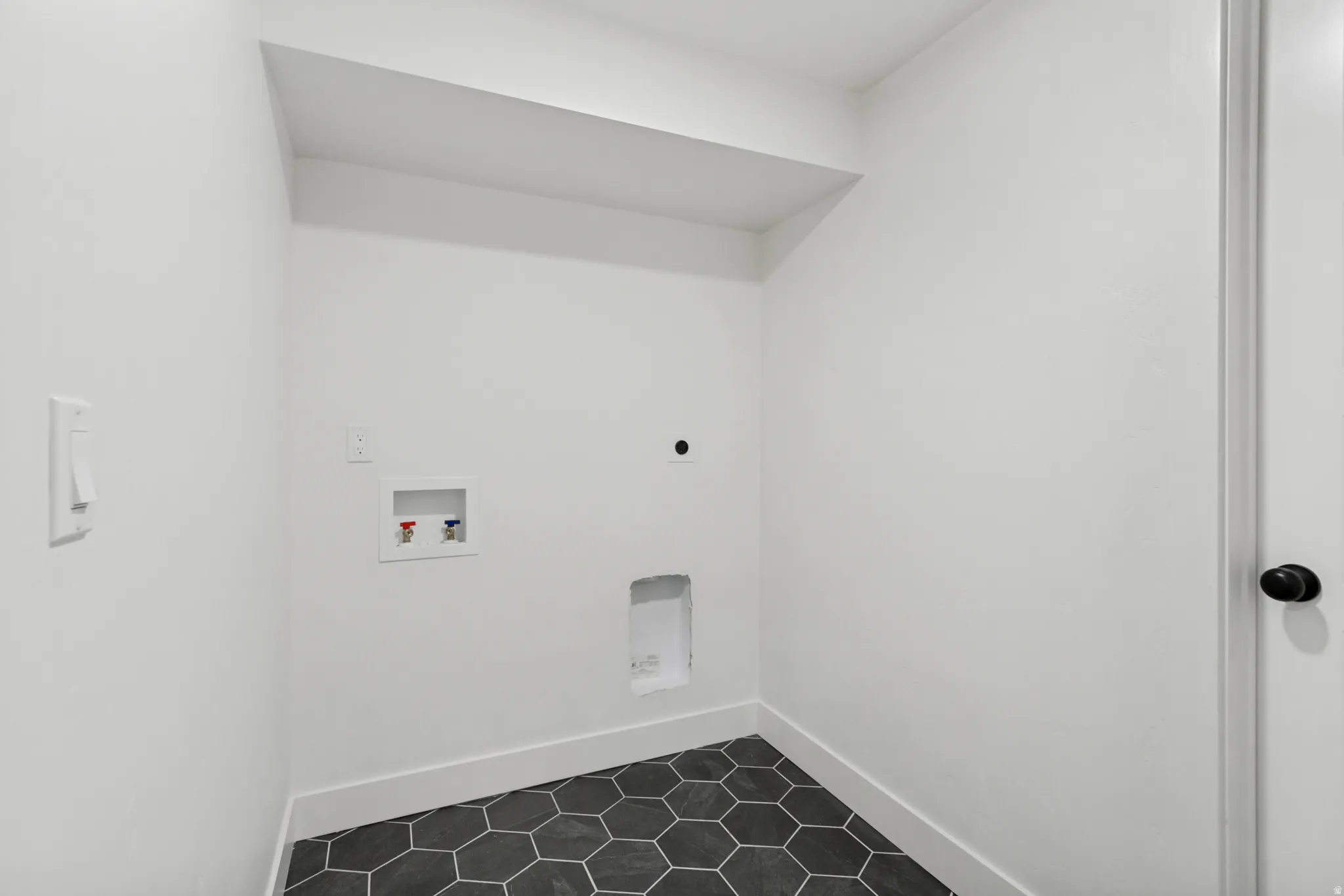 Dedicated laundry area featuring a white color palette, dark hexagonal floor tiles, and a white baseboard trim