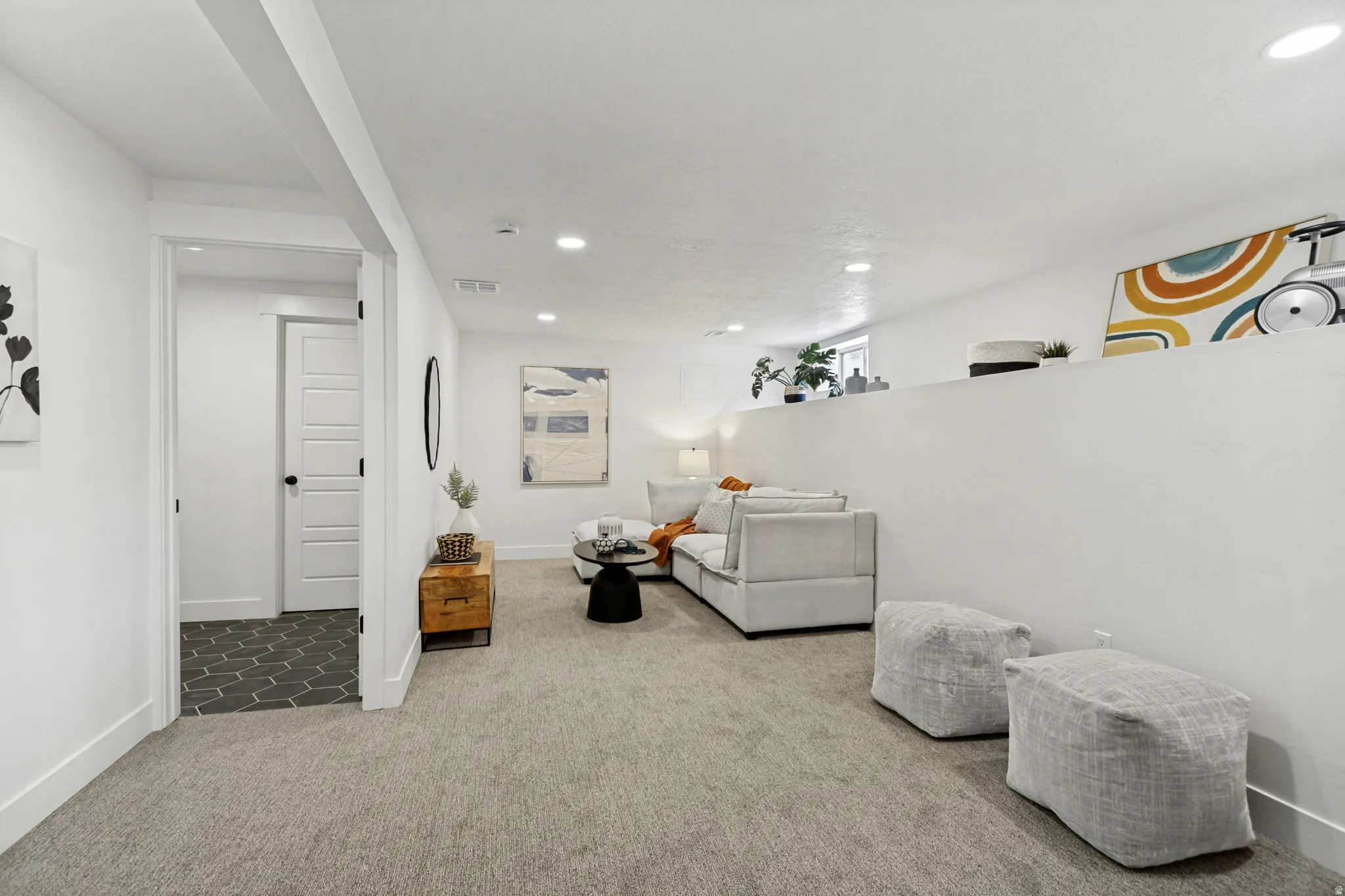 Carpeted recreation area with recessed lighting, a half-wall partition, and a doorway opening to a dark hexagonal tile floor