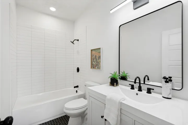 Bathroom featuring a single vanity with an integrated sink, matte black fixtures, a rectangular framed mirror, and a full bathtub with white subway tile surround