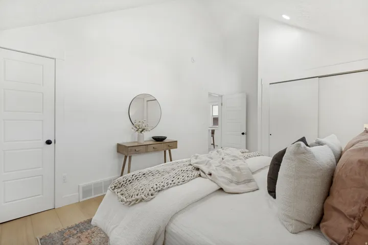 Vaulted ceiling bedroom featuring white walls, five-panel interior doors with black hardware, wood-finish flooring, and sliding closet doors