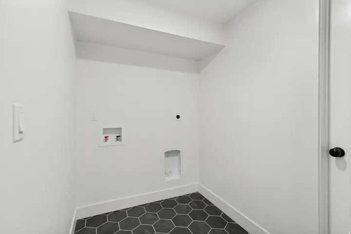 Dedicated laundry area featuring a white color palette, dark hexagonal floor tiles, and a white baseboard trim