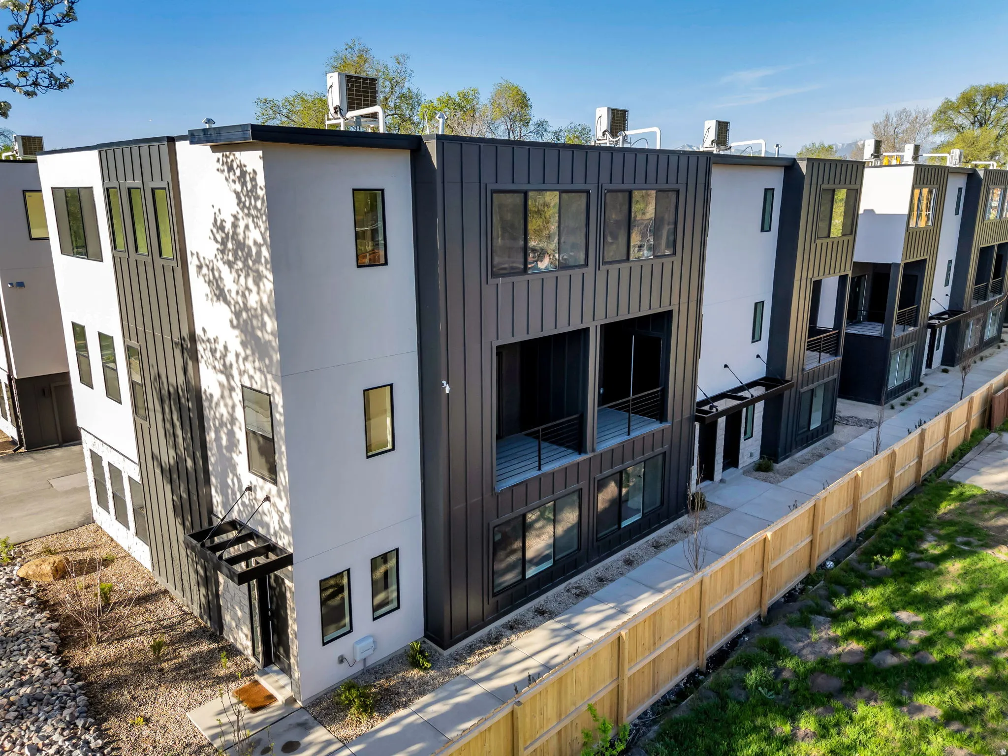 Modern multi-level townhome featuring a black and white facade with vertical siding accents, multiple floor-to-ceiling windows, and a private balcony