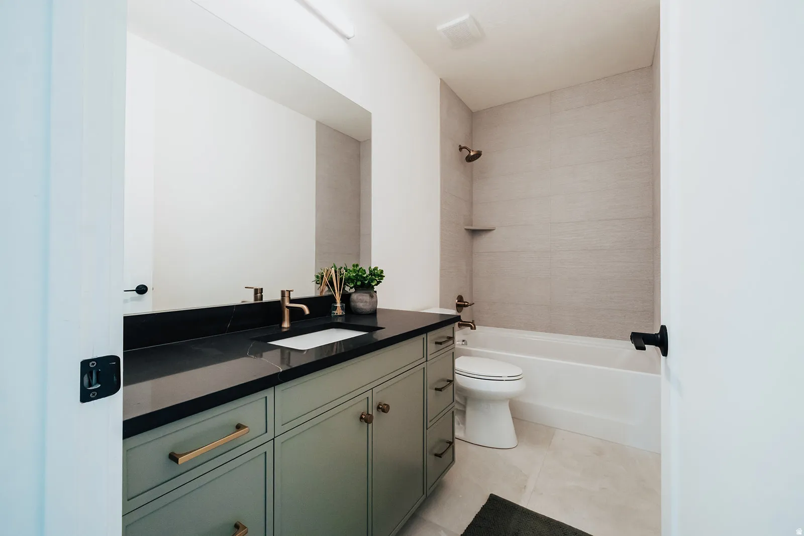 Full bathroom featuring a sage green vanity with gold hardware, a dark countertop, an undermount sink, and a large mirror