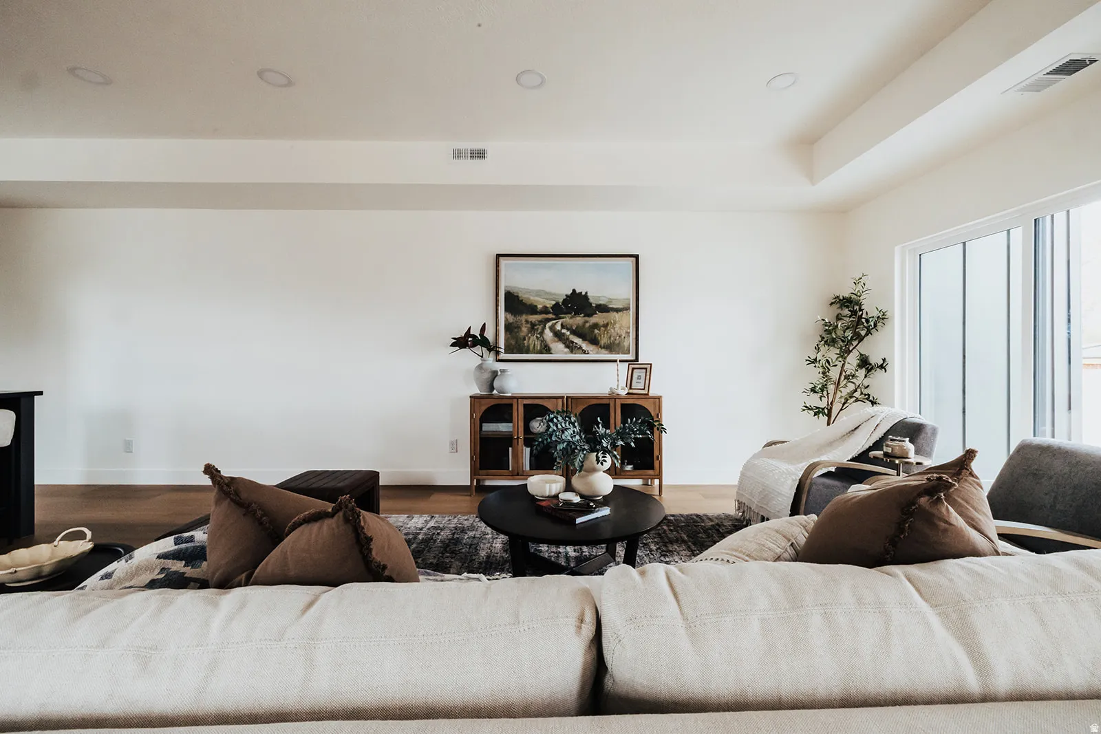 Spacious living area featuring light-colored walls, recessed ceiling lighting, wood-finish flooring, and a large sliding glass door