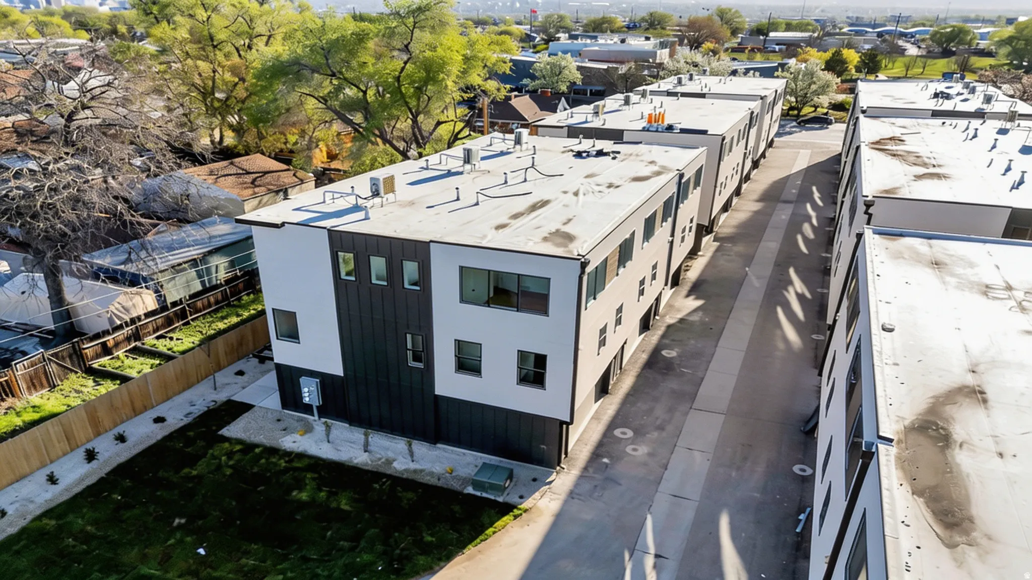 Modern multi-unit development featuring a two-tone facade, flat roofline, multiple windows, and individual yard spaces