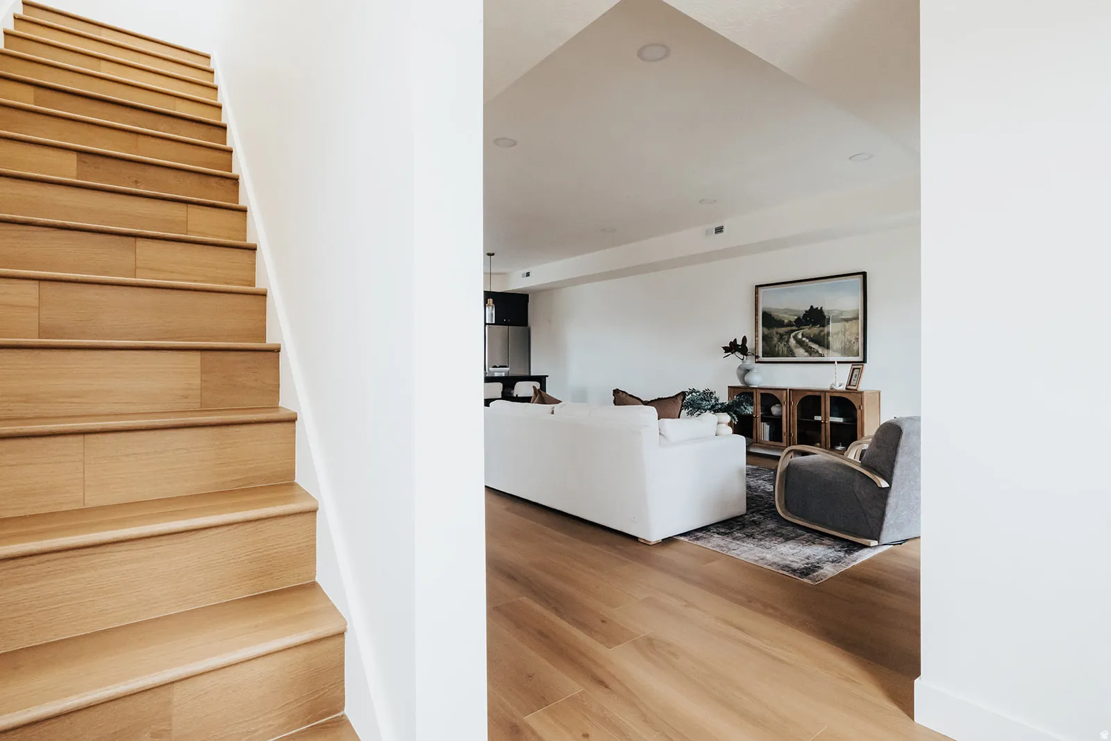 Wood-finish staircase with white risers and handrail, complementing the wood-finish flooring visible in the adjacent living area