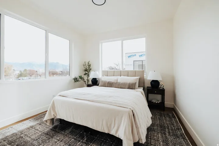 Bright bedroom featuring large windows, wood-finish flooring, and a flush-mount ceiling light fixture