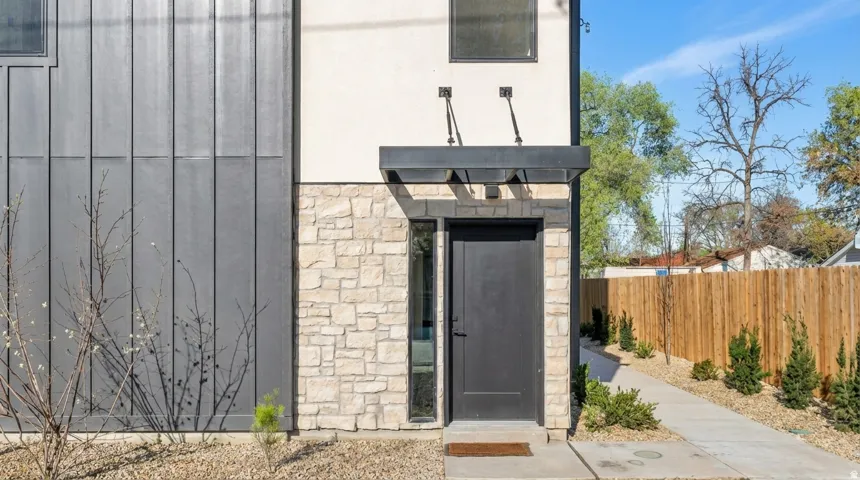 Modern exterior featuring vertical metal siding, stacked stone accents, a dark entry door, and a covered entryway