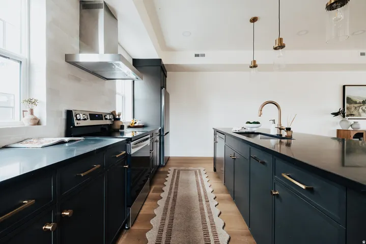 Modern kitchen featuring dark cabinetry with brass hardware, stainless steel appliances, and a central island with a gold-finish faucet