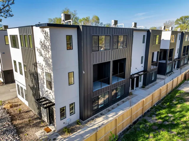 Modern multi-level townhome featuring a black and white facade with vertical siding accents, multiple floor-to-ceiling windows, and a private balcony