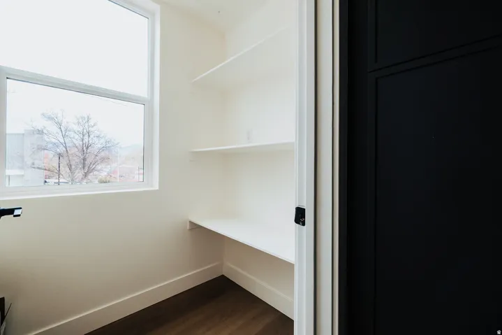 Dedicated pantry space featuring a white frame window, multiple floating shelves, and wood-finish flooring