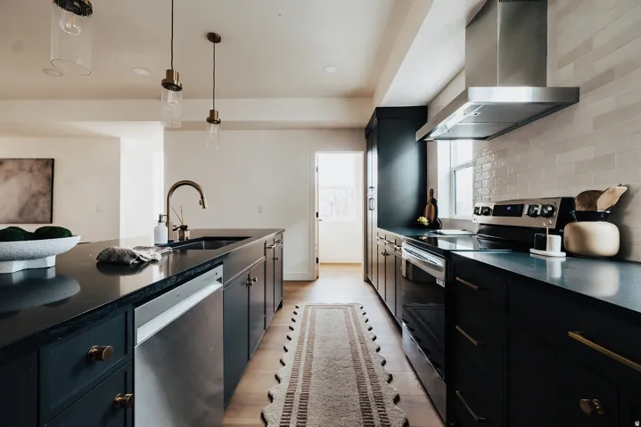 Gourmet kitchen featuring dark cabinetry, dark countertops, an undermount sink with a gooseneck faucet, stainless steel appliances, and wood-finish flooring