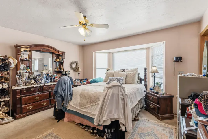 Bedroom featuring a multi-pane bay window, ceiling fan with integrated lighting, textured ceiling, and neutral wall tones
