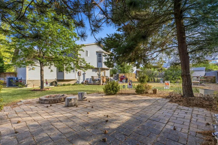 Expansive backyard featuring a paver patio with a built-in fire pit, mature trees, and a manicured lawn