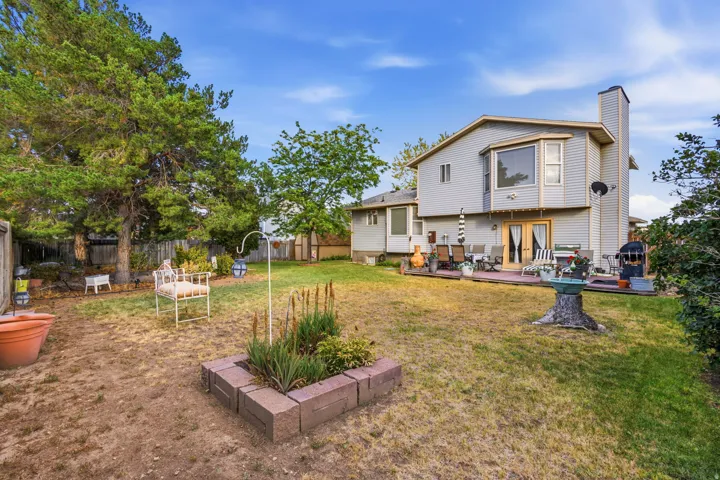 Spacious backyard featuring a multi-level deck, mature trees, a block-edged garden bed, and wood fencing