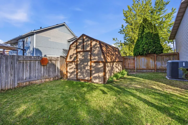 Fenced backyard featuring a gambrel-style storage shed, established lawn, and mature perimeter trees