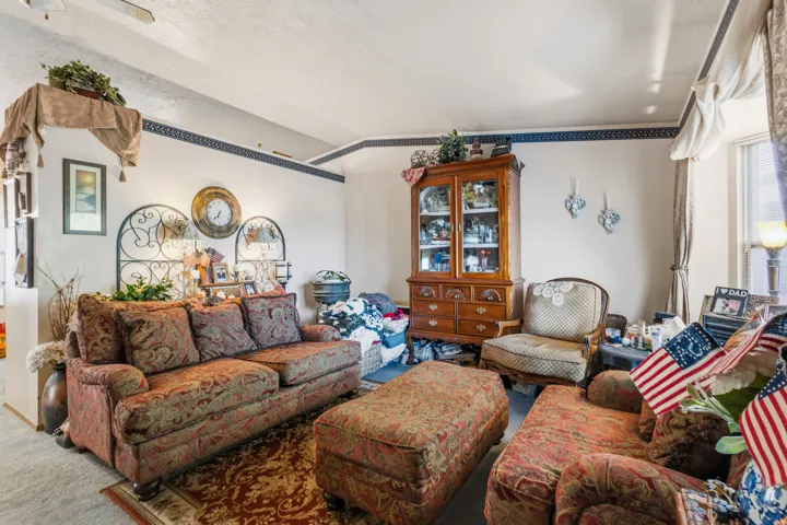 Living area featuring textured walls with decorative border, wood-finish display cabinet with glass doors, and a window with drapery